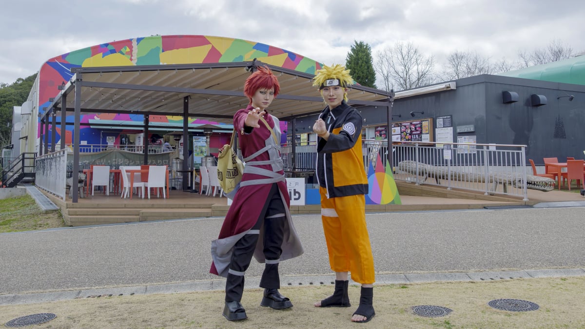 Two cosplayers as Gaara and Naruto from Naruto, posing at an outdoor venue.