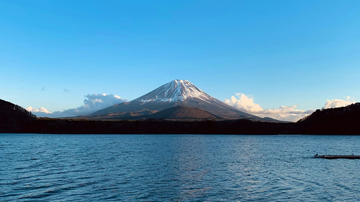 Mount Fuji reflected across Lake Motosu with a small boat visible on the water