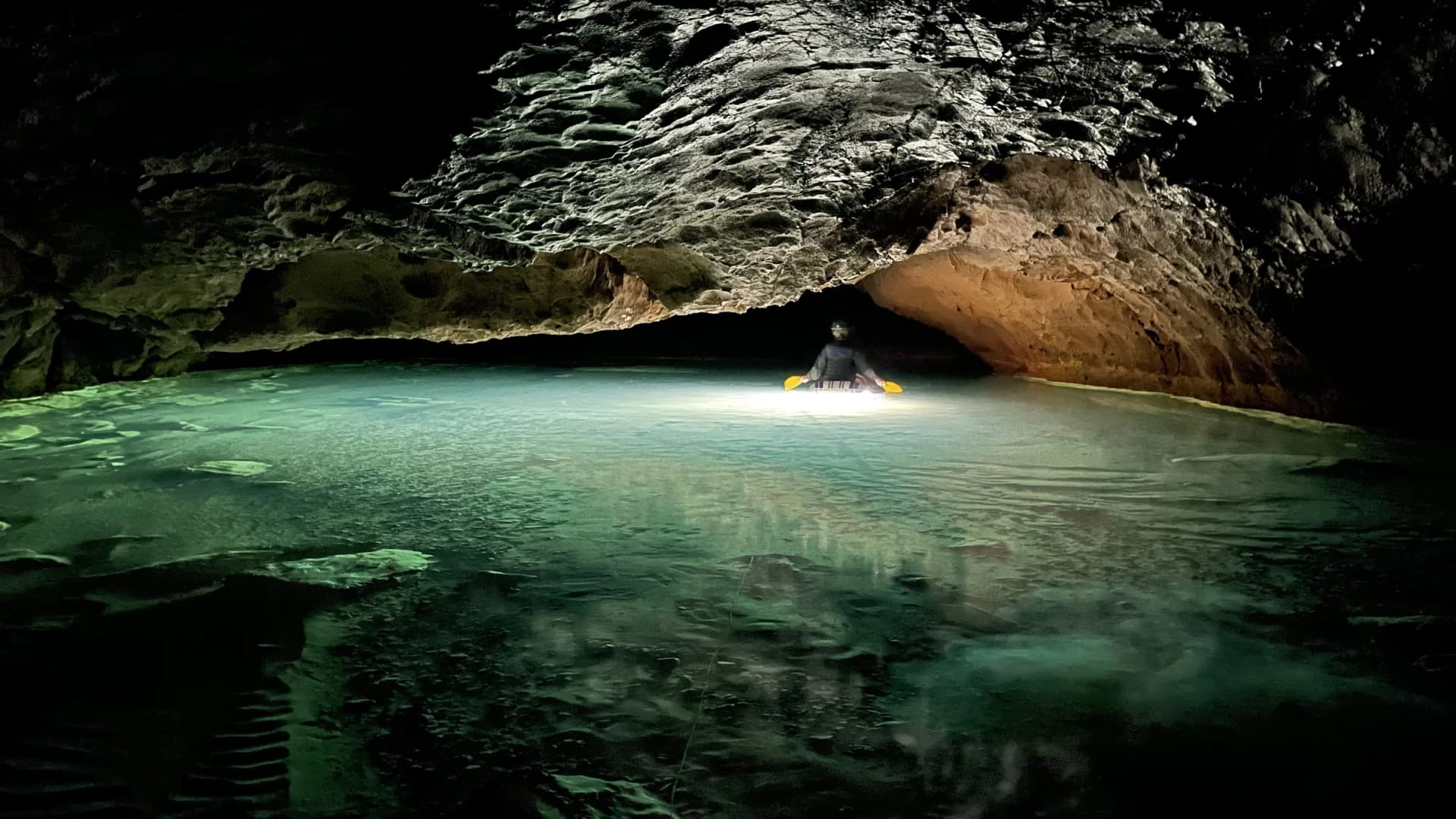 A caver paddles through an emerald underground pool in the unlit depths of Akiyoshido Cave, Yamaguchi