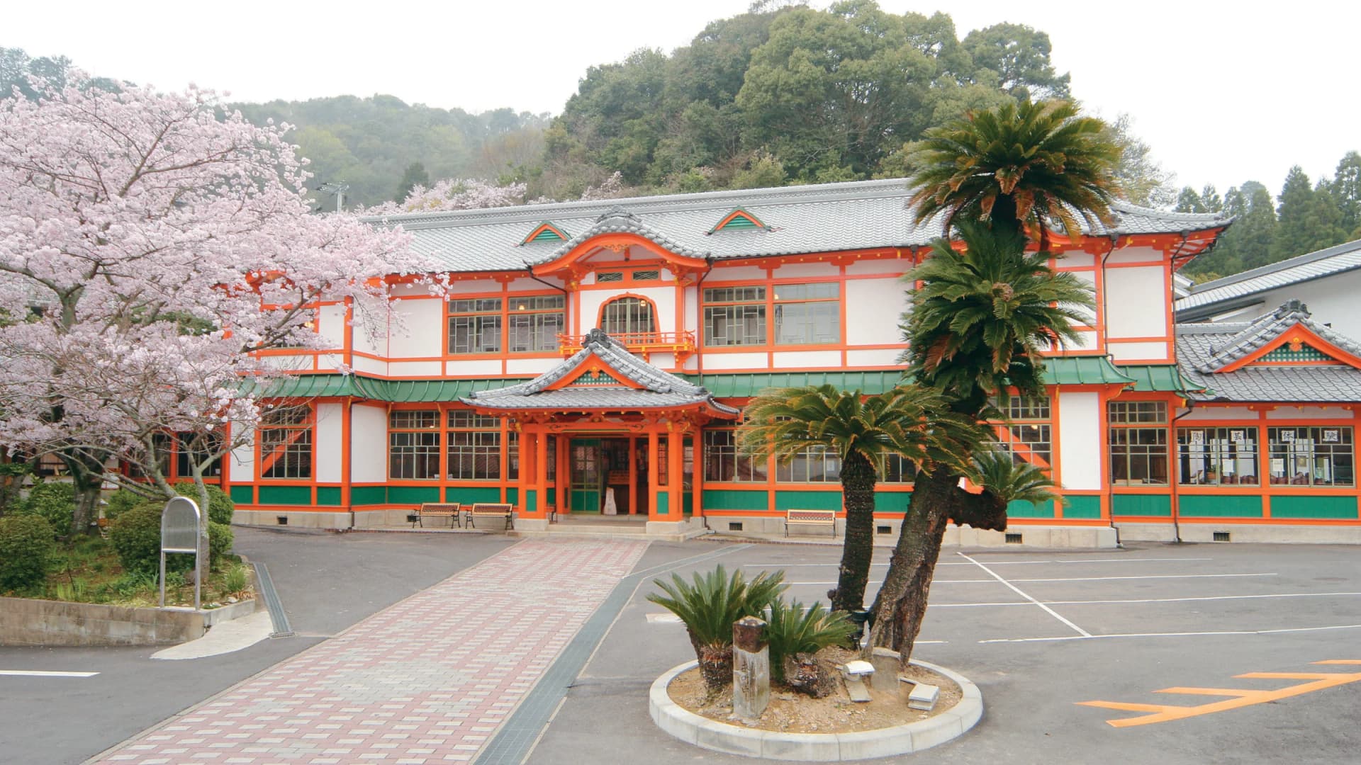 Cherry blossoms frame the vermilion Shinkan bathhouse at Takeo Onsen, Saga