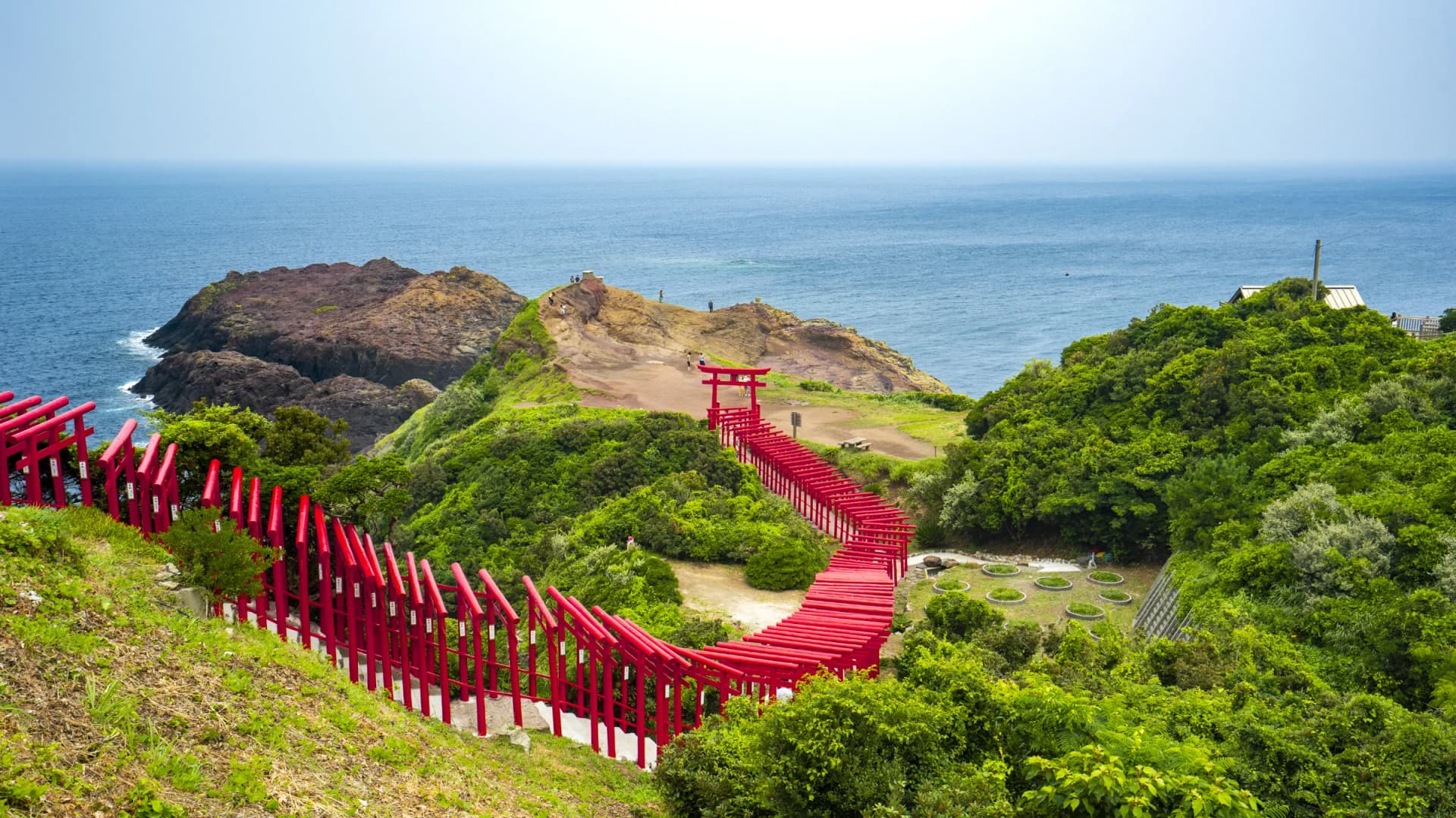 A winding path of red torii gates descends toward the sea at Motonosumi Shrine, Yamaguchi