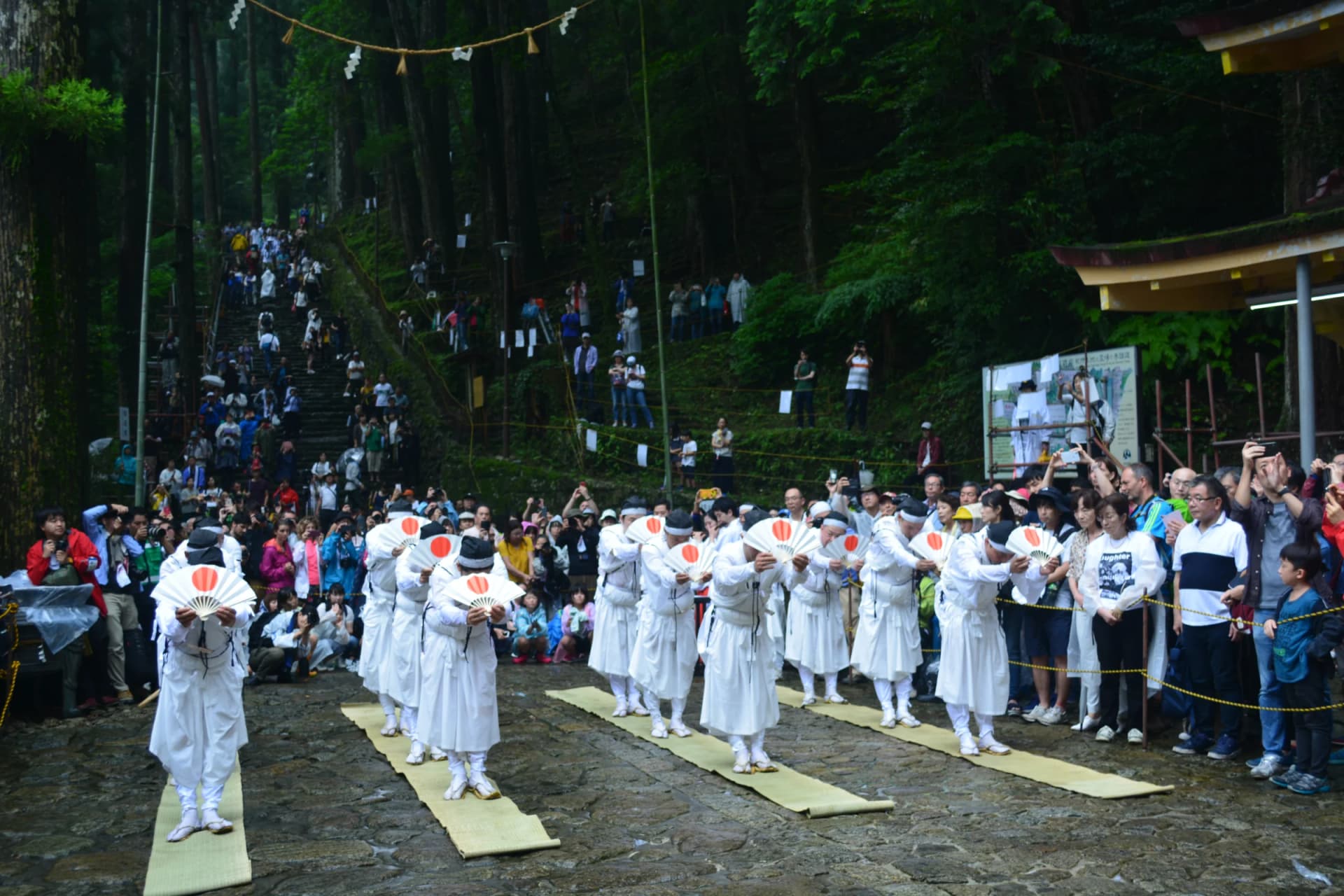 Priests in white bow with rising-sun fans before the crowds at the Nachi Fire Festival, Wakayama
