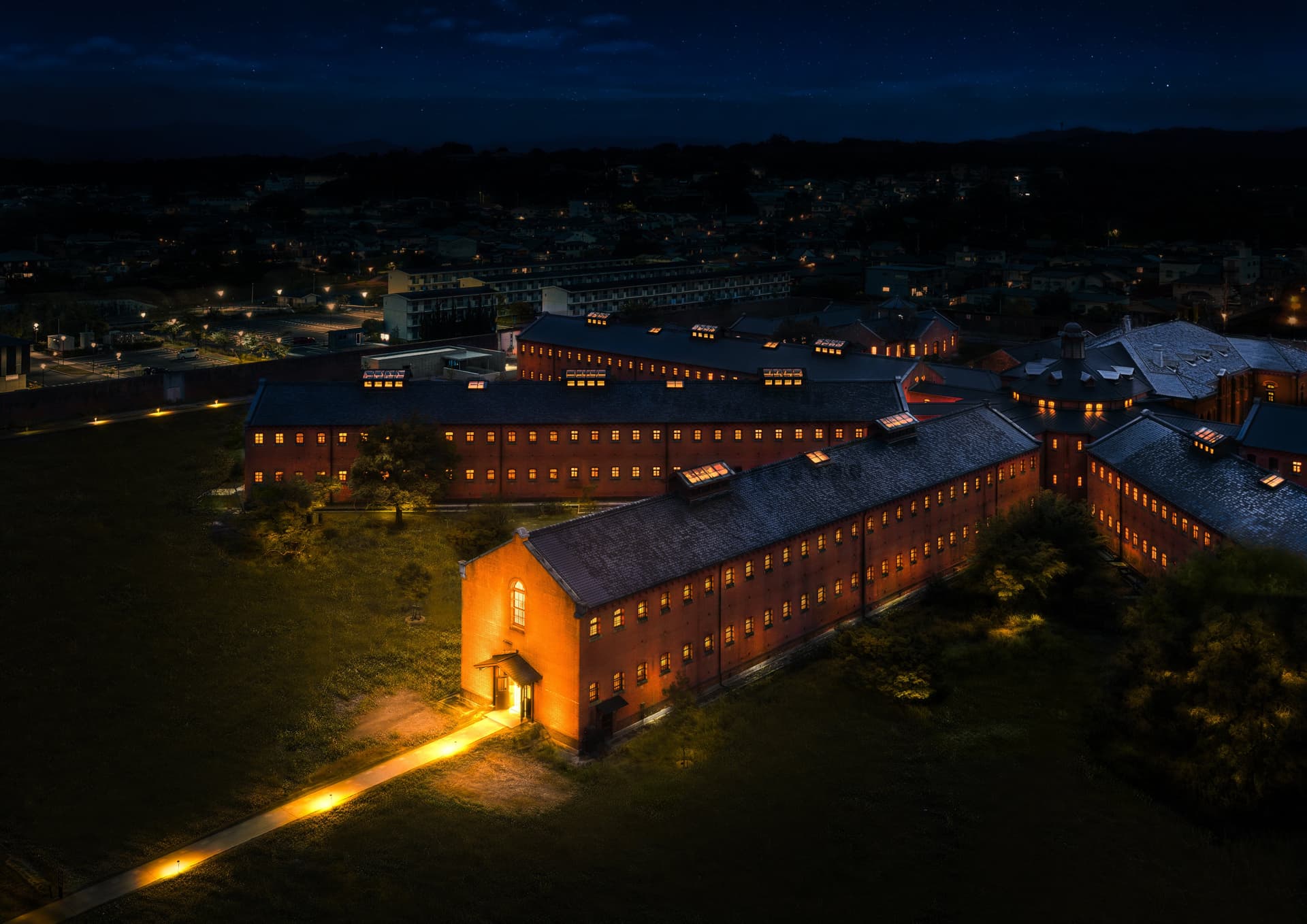 Aerial night view of the lit red-brick wings of the former Nara Prison