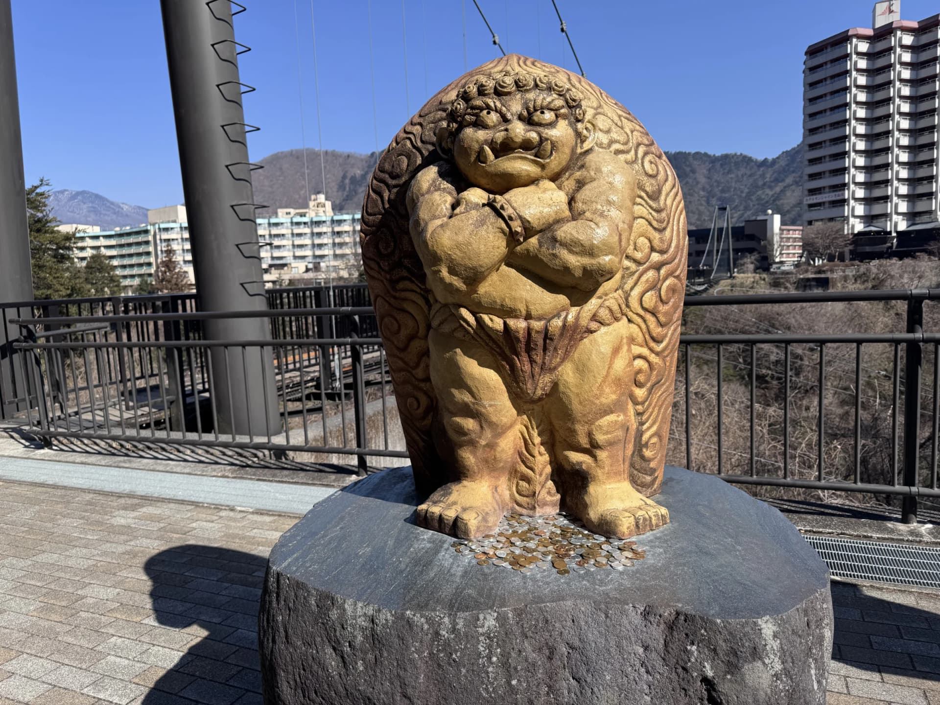 An oni statue with coins left at its feet, beside the suspension bridge at Kinugawa Onsen, Nikko, Tochigi