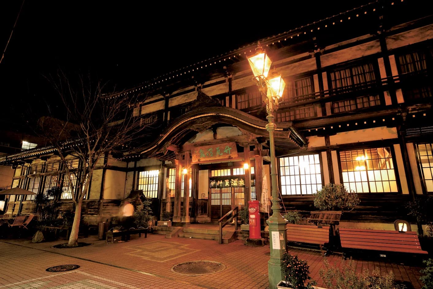 Retro gas lamps light the wooden entrance of Takegawara Onsen after dark, Beppu, Oita