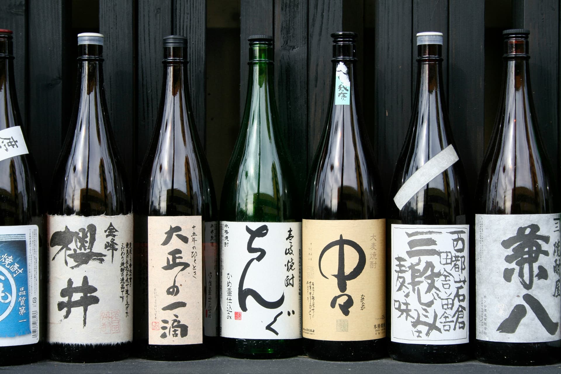A row of isshobin bottles of honkaku shochu with hand-lettered labels.