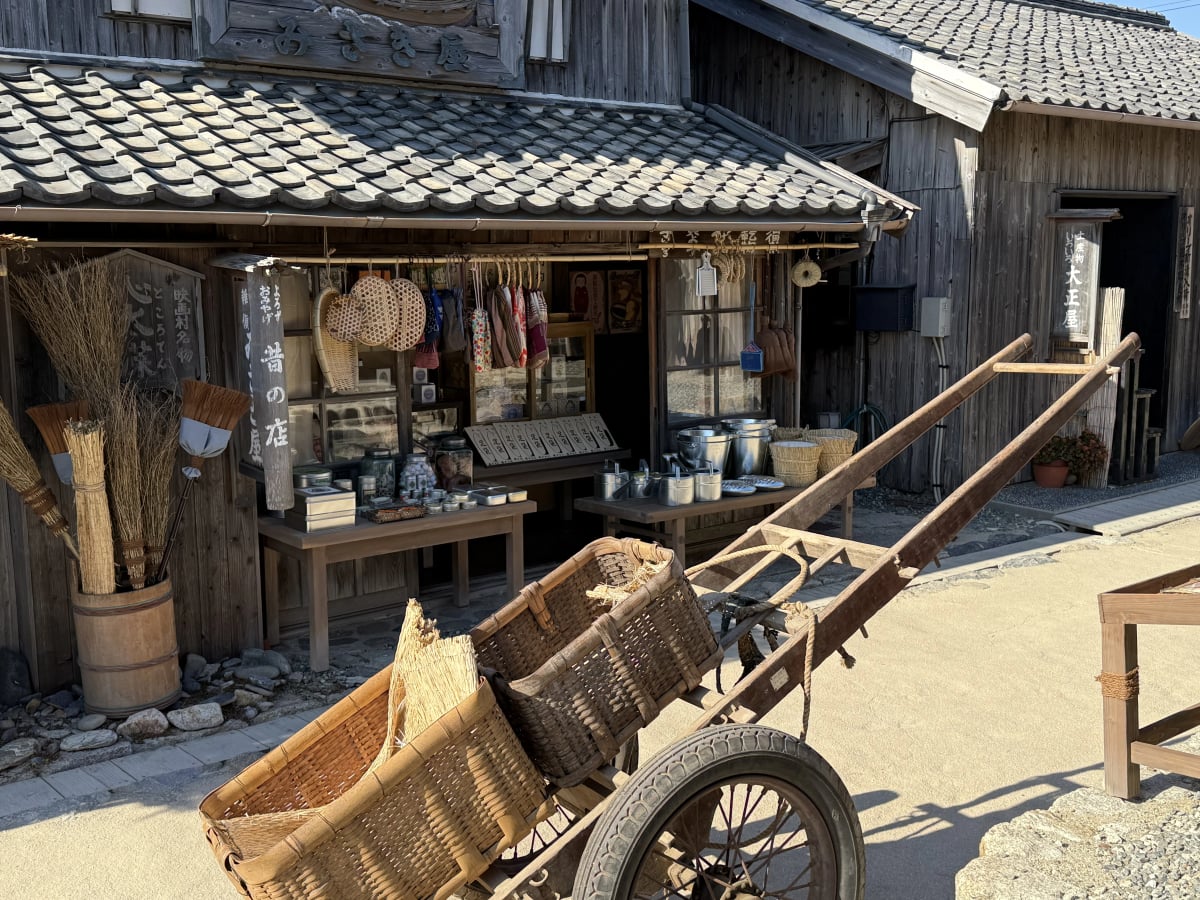 The village's nostalgic shopping street, lined with recreated storefronts and a hand-pulled cart reminiscent of daily life in early Showa-era Japan, at Twenty-Four Eyes Movie Village