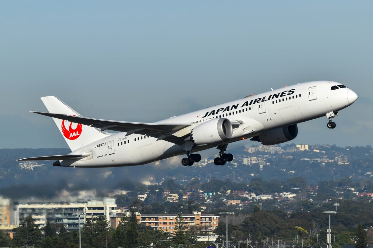 Japan Airlines Boeing 787 Dreamliner aircraft in flight over a suburban landscape.